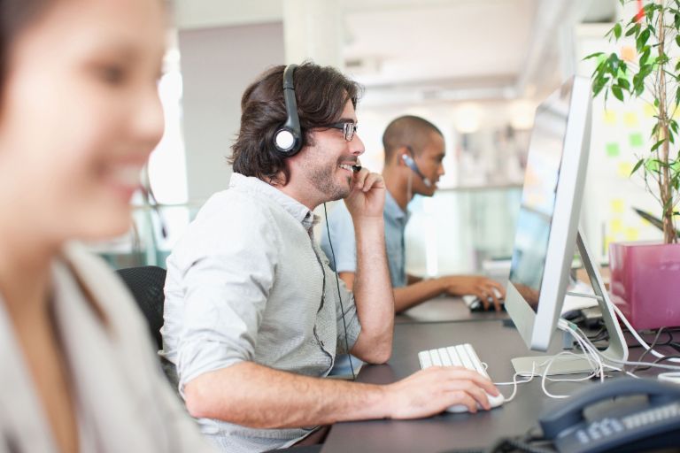 Foto von Callcenter-Mitarbeitern, die mit Headsets am Computer telefonieren.