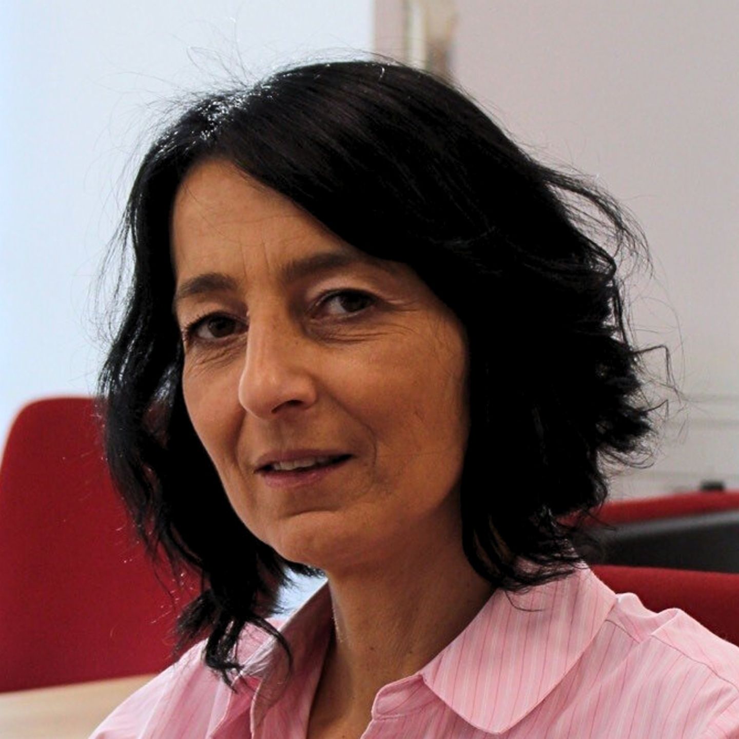 Cristina Pasere, Managerin Compliance Operations Support, EOS Rumänien sitzt in rosa gestreifter Bluse am Schreibtisch und guckt in die Kamera