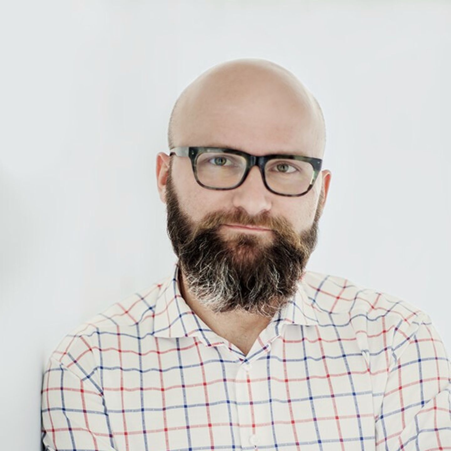 Dr. hab. Tomasz Piekot in einem karierten Hemd lehnt an einer weißen Wand.