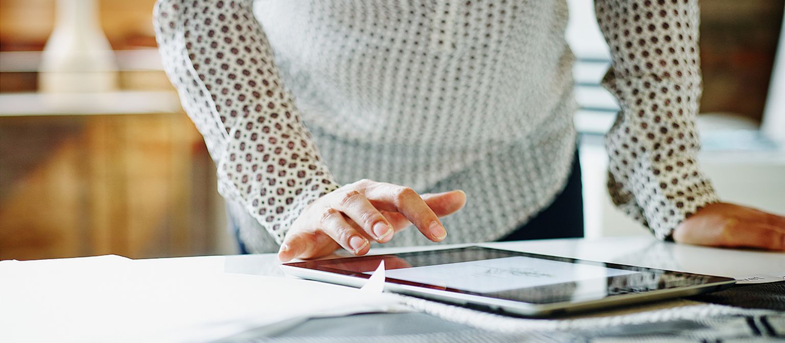 Frau steht am Schreibtisch und tippt auf ihrem Tablet
