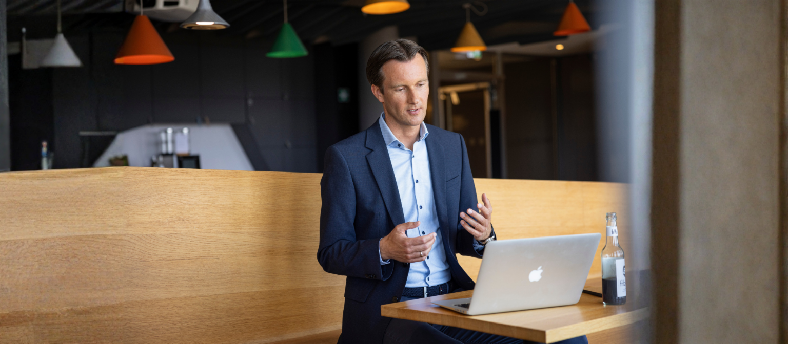 Carsten Tidow sitzt mit aufgeklapptem Laptop auf einer Bank und gestikuliert, während er erklärt.