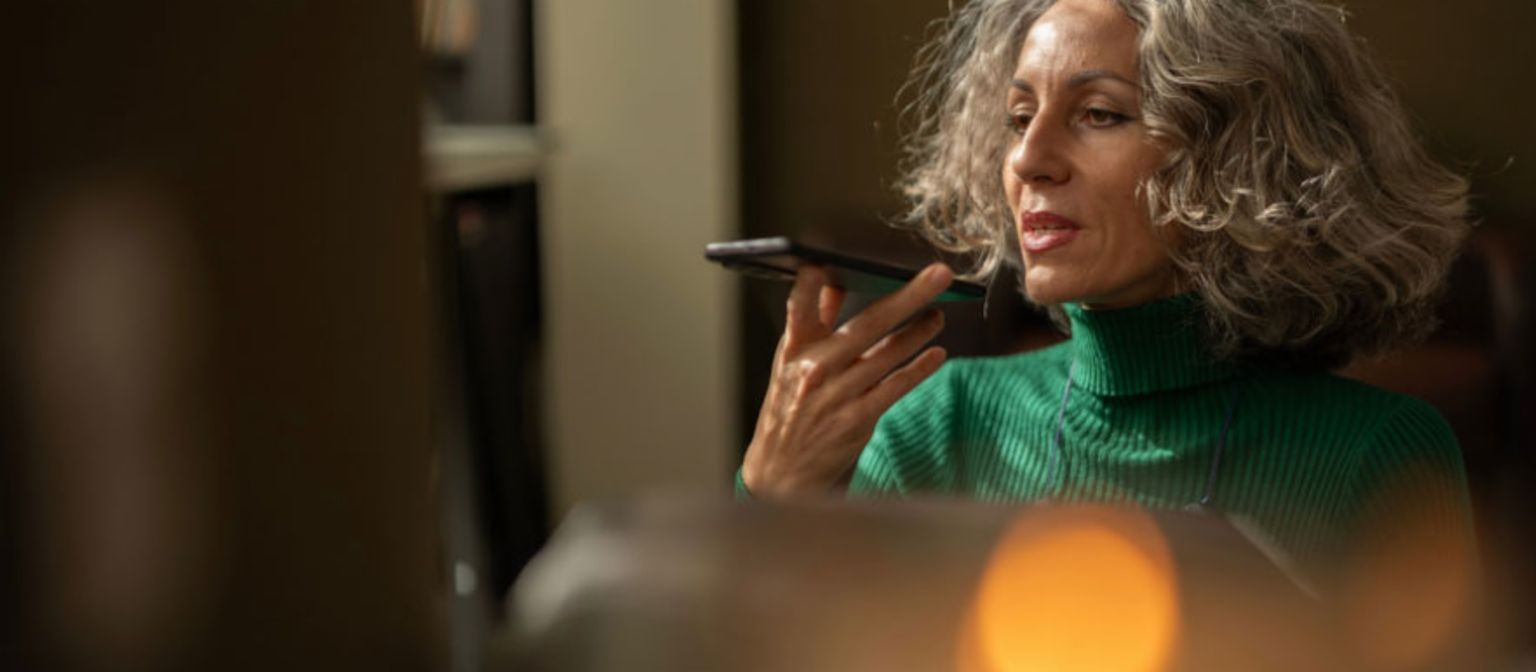 Eine Frau mit einem Mobiltelefon in der Hand spricht mit der KI.
