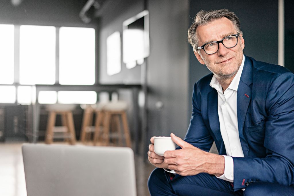 Was ist Forderungsverkauf: Geschäftsmann sitzt in Lobby und trinkt Kaffee. 