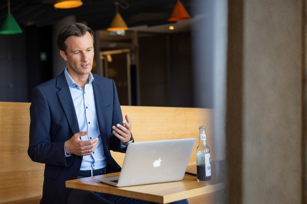 Carsten Tidow sitzt mit aufgeklapptem Laptop auf einer Bank und gestikuliert, während er erklärt.