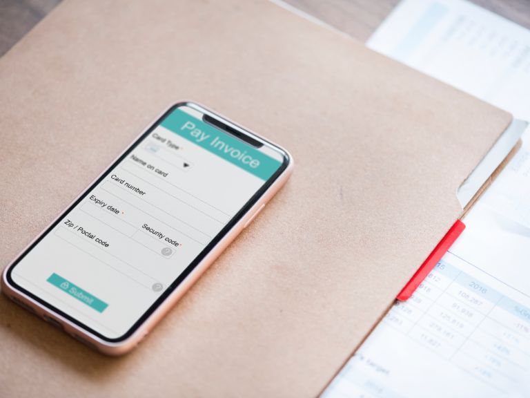Mobile phone with open app for payment lies on file folder with invoice.