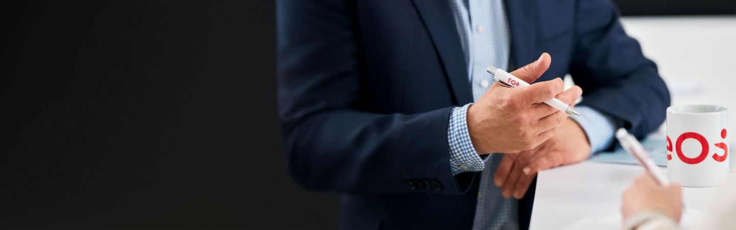 Geschäftsmann hält EOS-Stift während eines Gesprächs über internationales Forderungsmanagement, EOS-Tasse auf dem Tisch - Expertise in Inkasso, NPLs und digitale Lösungen