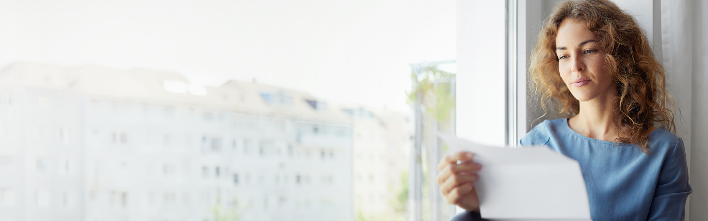 Woman reading a letter sitting on a window at home