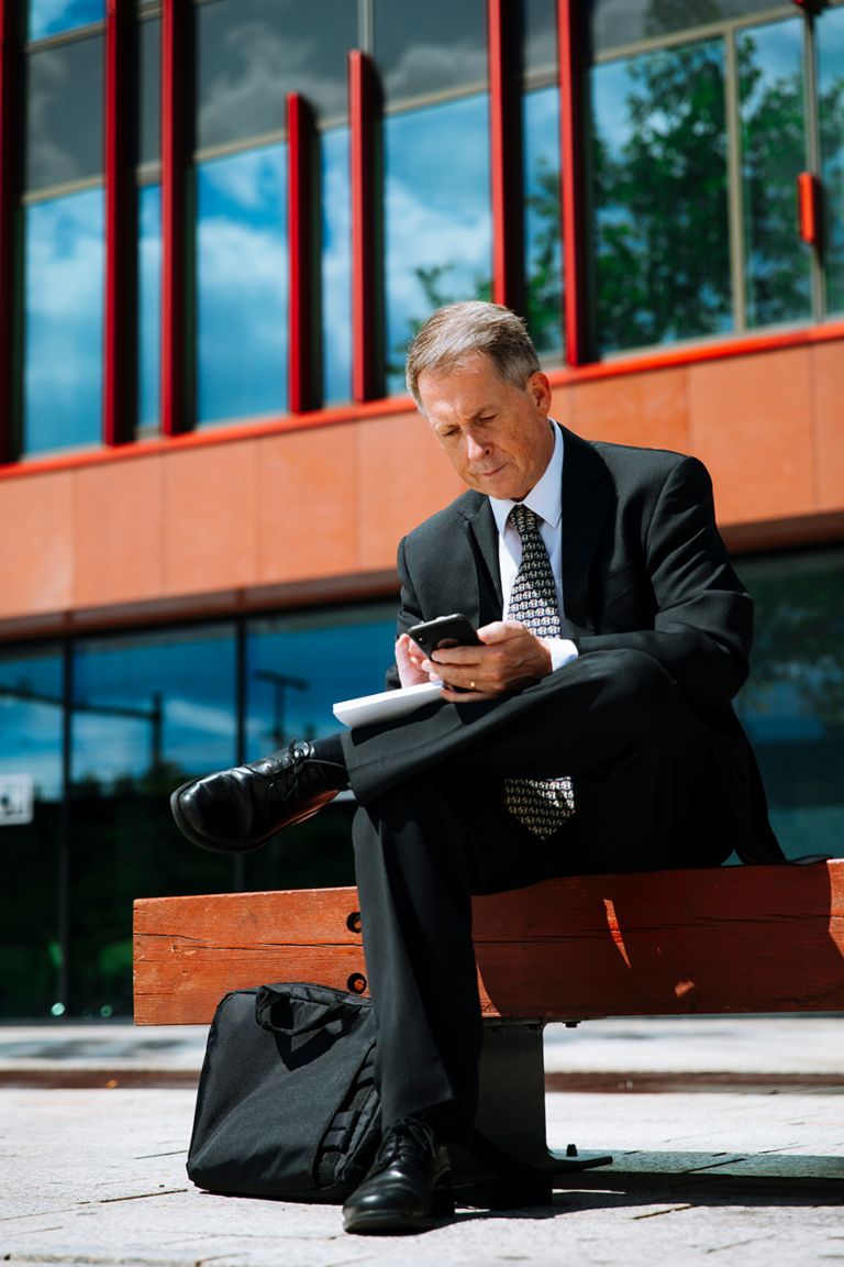 Internationales Inkasso: Raymond Pappot sitzt auf einer Bank und schaut auf sein Smartphone.