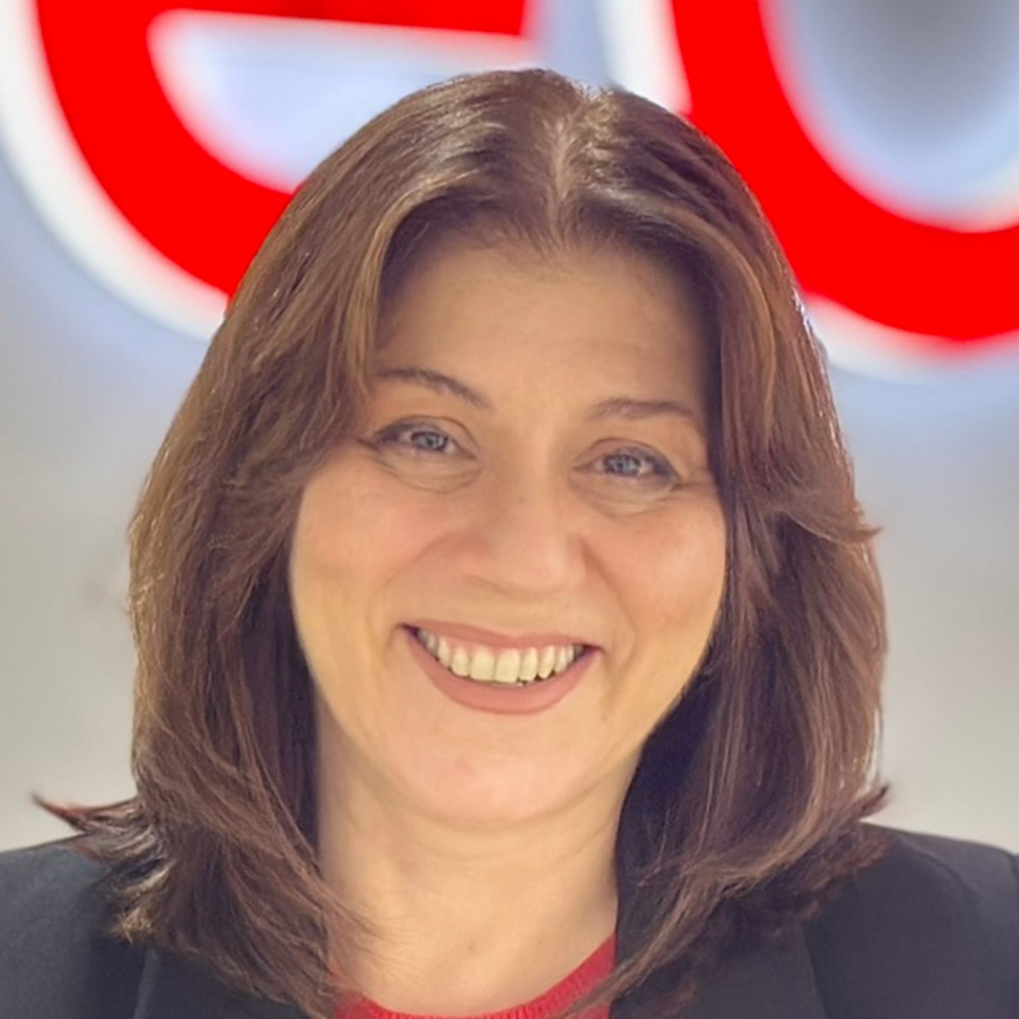 Belén Barreiro, Contact Center Agent bei EOS in Spanien lehnt vor leuchtendem EOS Logo im schwarzen Blazer an einem Tresen. 