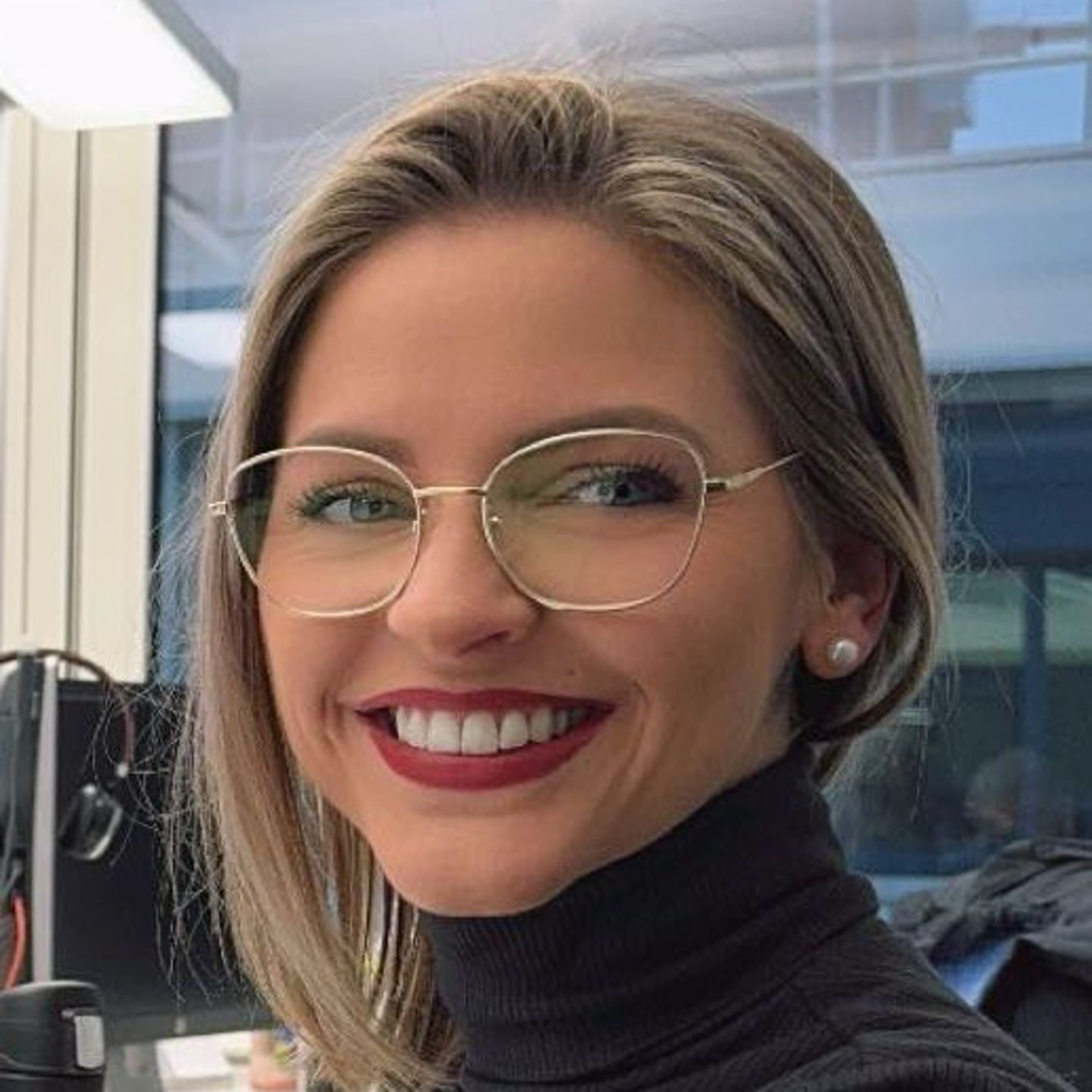 Genny Bollinger, Debt Restructoring Specialist EOS in der Schweiz, sitzt in grauem Rollkragen-Pullover am Schreibtisch und lächelt in die Kamera 