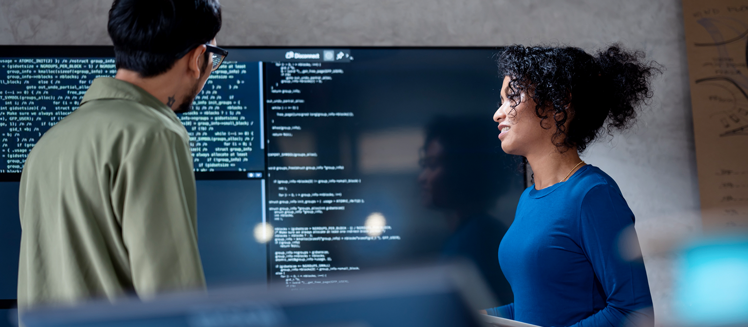 KI im Forderungsmanagement: In diesem Bild analysieren zwei Fachleute gemeinsam Programmiercode für automatisierte Prozesse auf einem großen Bildschirm. Die Szene veranschaulicht die praktische Anwendung von Künstlicher Intelligenz (KI) und Robotic Process Automation (RPA) im Forderungsmanagement – ein Beispiel für die digitale Transformation im Forderungsmanagement.