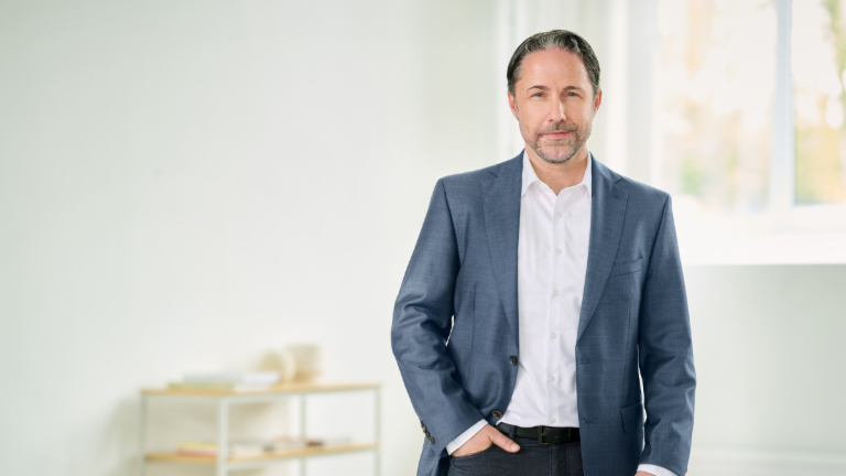Marwin Ramcke, CEO, steht mit blauem Anzug und der rechten Hand in der Hosentasche in einem hellen Raum. 