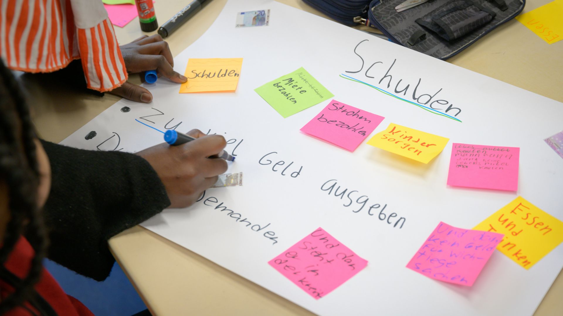 Finanzbildung für Kinder: Kinder basteln ein Plakat zum Thema Schulden.