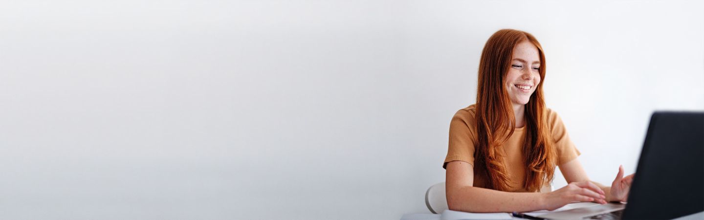 Young woman with red hair sits at the desk at the laptop.