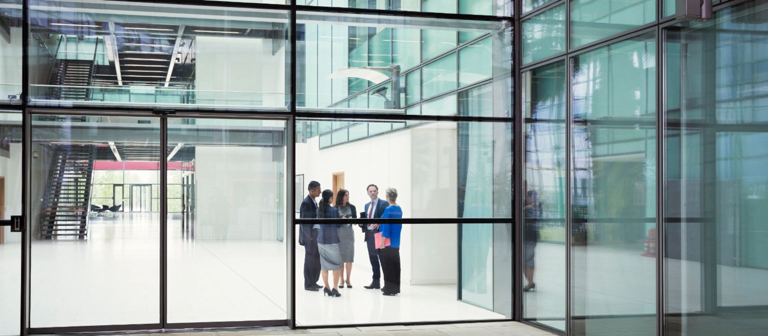 Verkauf problembehafteter Immobilien-Portfolios: Menschen stehen im Eingangsbereich eines Bürogebäudes.
