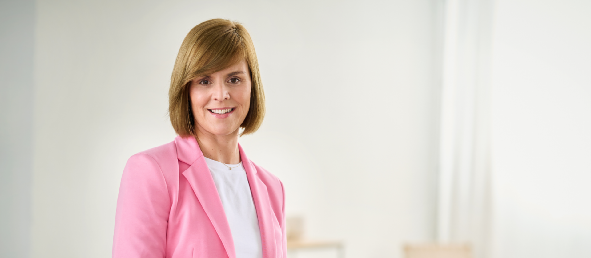 Eva Griewel, Frau mit rosa-farbenem Blazer und weißem Shirt steht in einem hellen Raum
