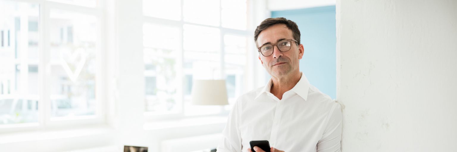 Businessman in white shirt holds a cell phone in his hand and looks thoughtfully to the side