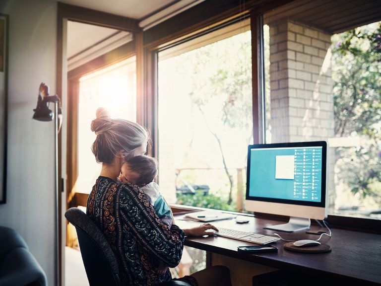 Einkommensabhängige Kredite: Eine Mutter sitzt mit ihrem Baby zuhause vor dem Computer.